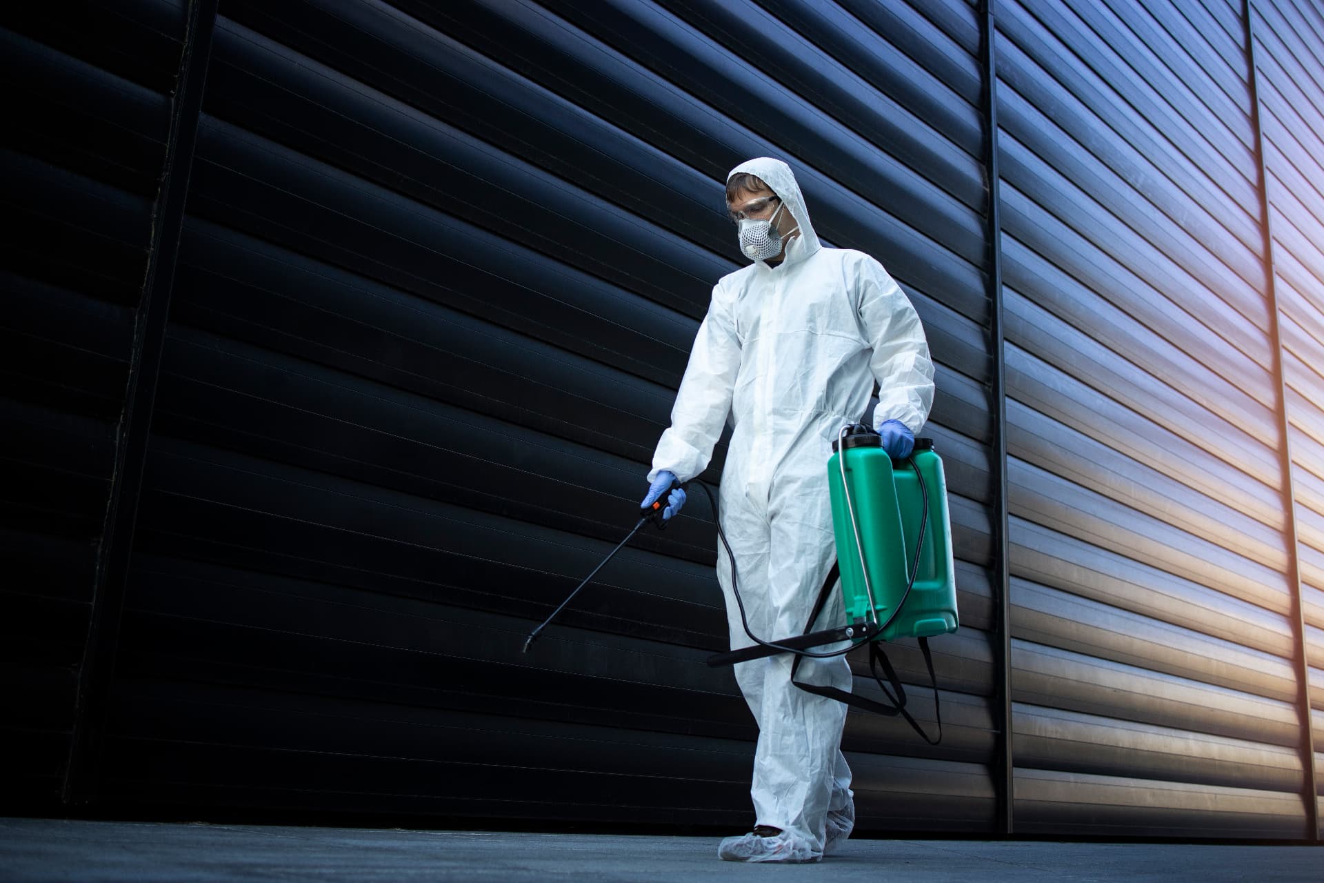Technician in full white chemical protection suit disinfecting public areas