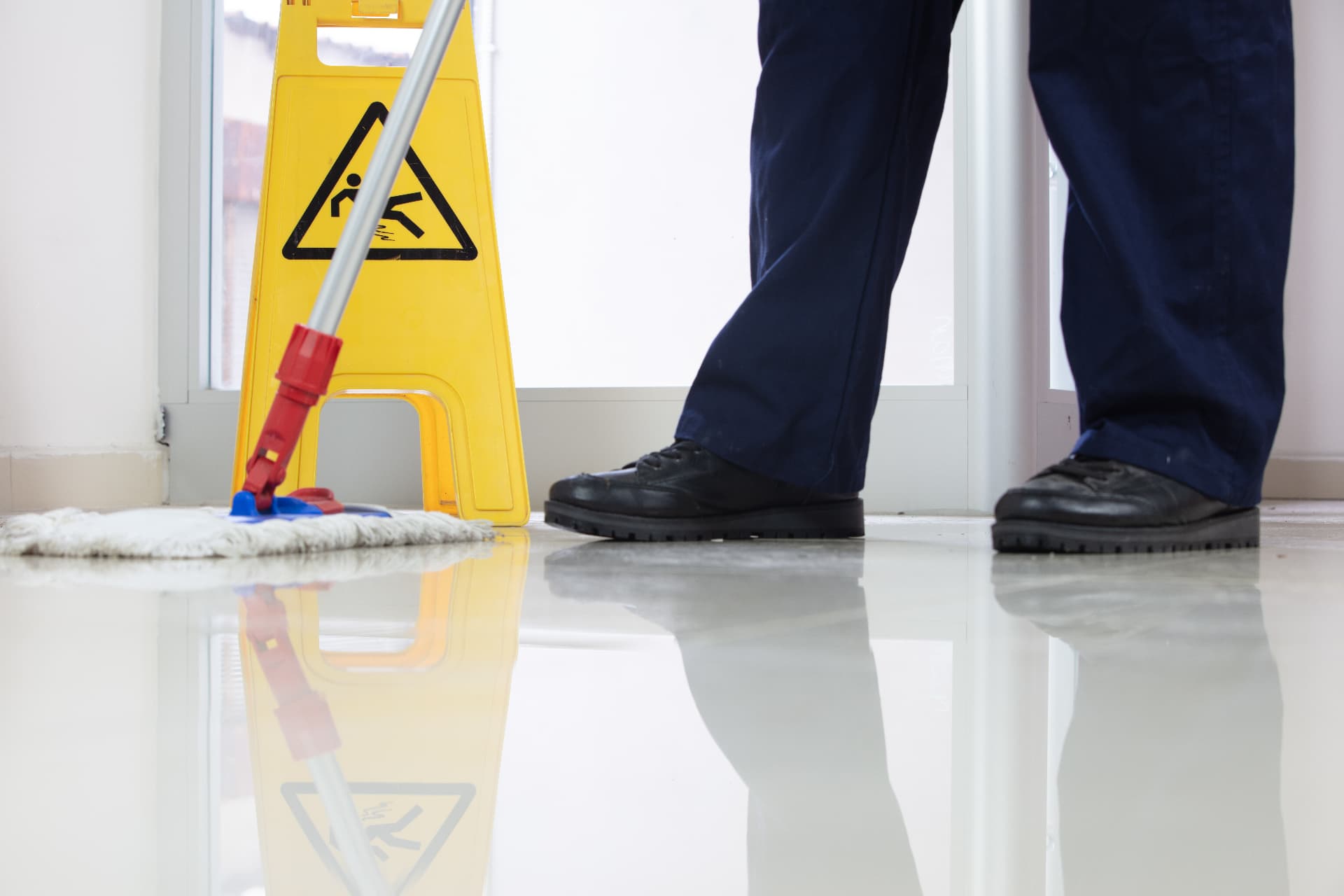 Cleaner mopping a shiny floor near a wet-floor caution sign